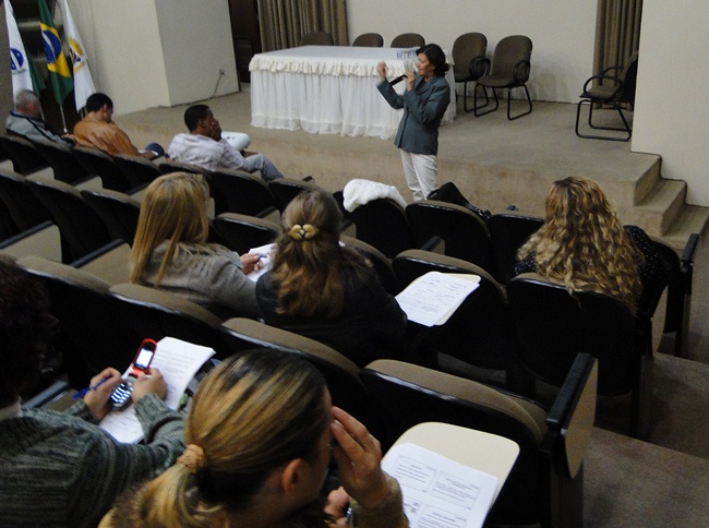 not Urânia Maria Ramos Tecnica do FNDE a frente de um palanque palestrando para um grupo pessoas sentados em um auditorio 