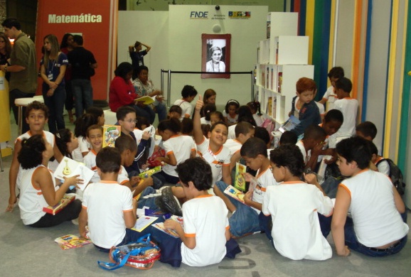 Crianças sentadas em circulo lendo, no estande do FNDE