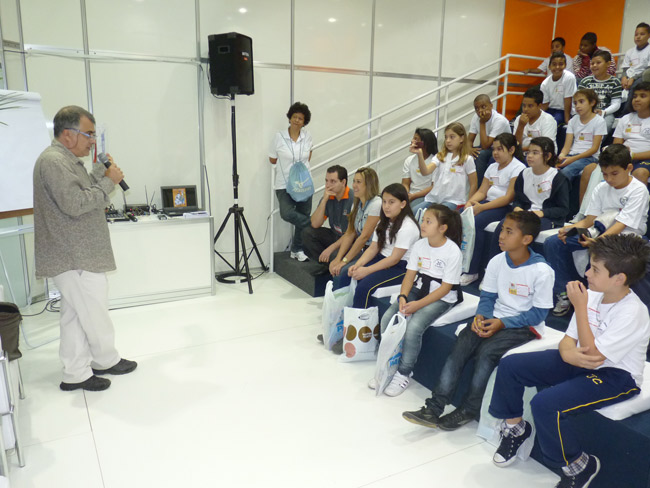 José Santos em pé palestrando para crianças sentadas em auditório