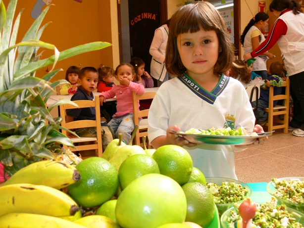 Criança com prato de comida junto à mesa com frutas